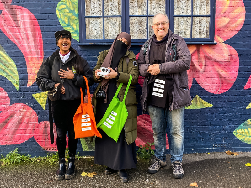 three people stand outside a house with colourful graffiti, they are laughing