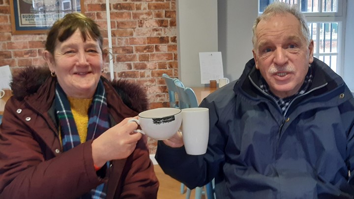 two older people laugh and cheers coffee cups