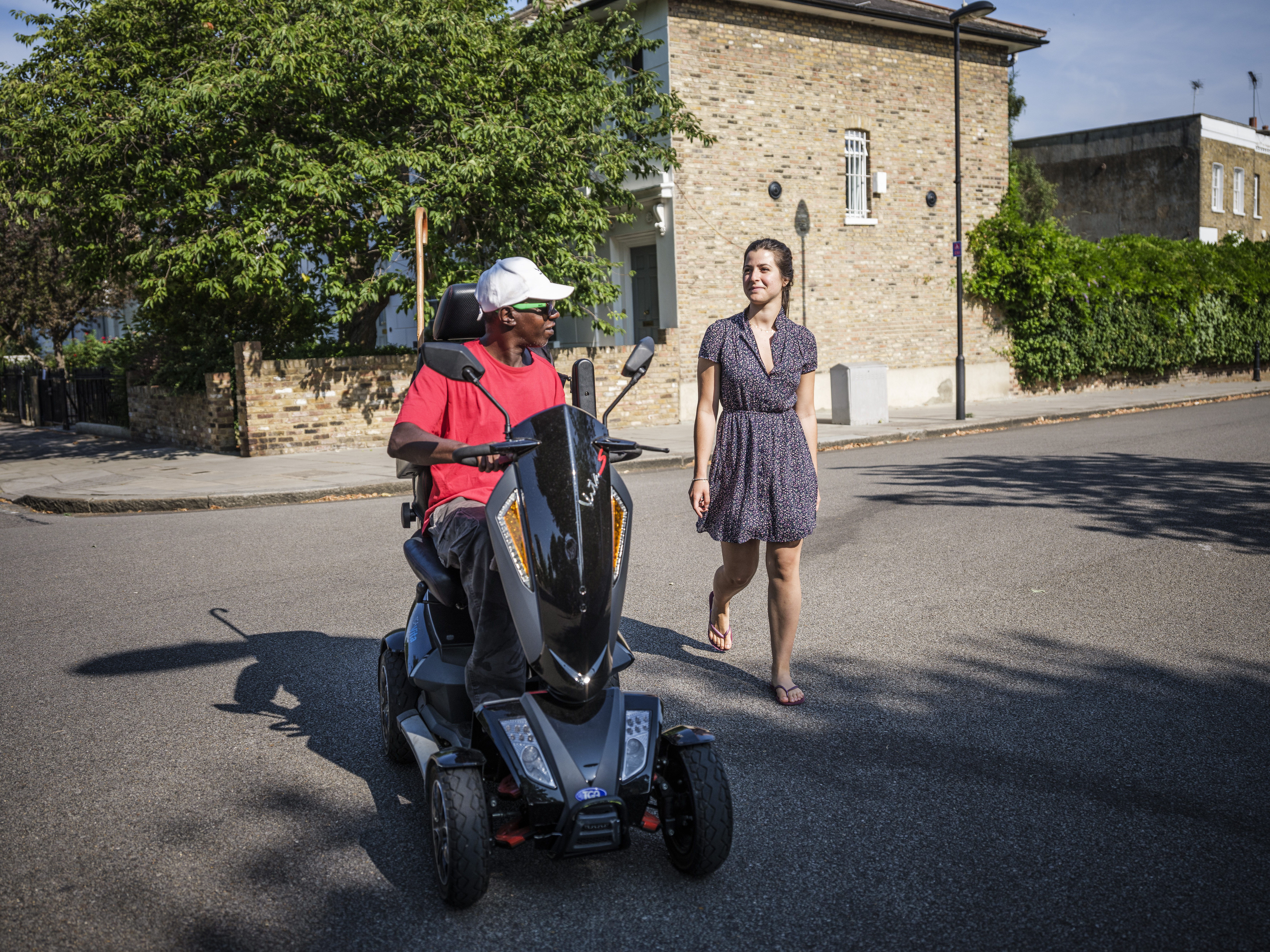 A man in a power assisted wheelchair and a woman walking