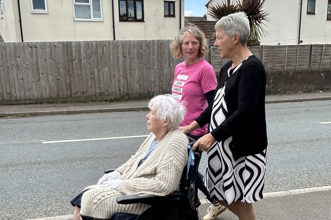 One person in a wheelchair with two people walking