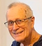 A photograph of Tony Pattison, an older white man. Tony is wearing black wire frame glasses and smiling at the camera.