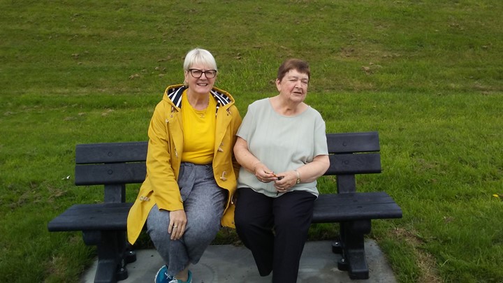 two older women sit on a park bench
