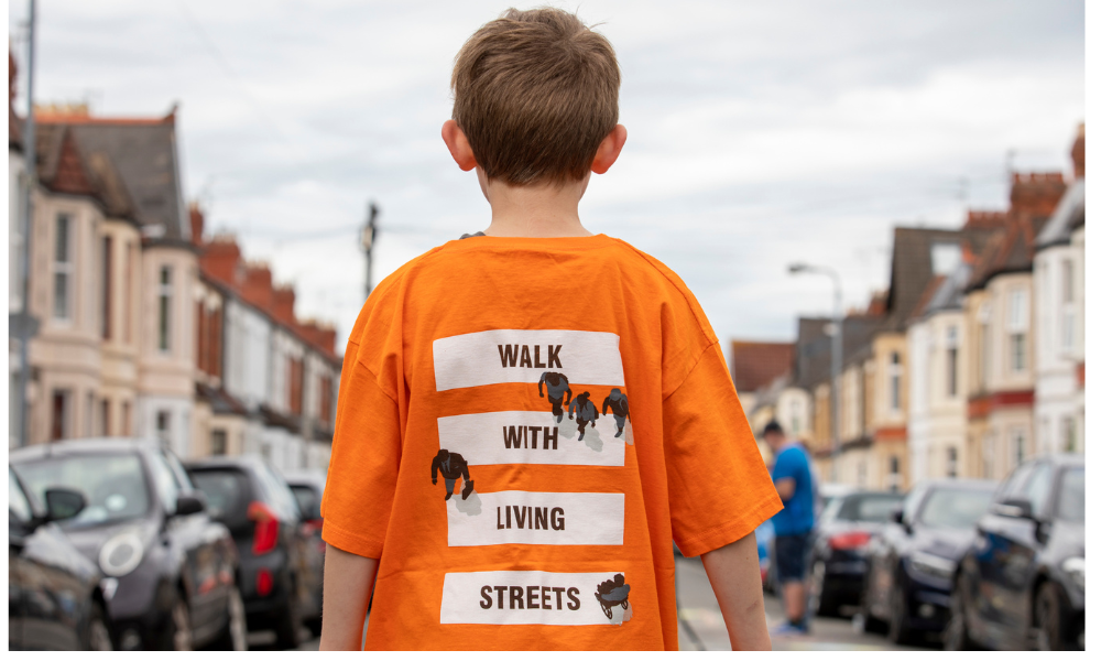 A photo of a child with their back to the camera. Their t-shirt has a Living Streets logo on with the words 'Walk with Living Streets'