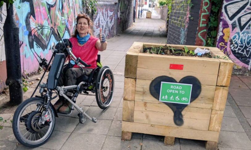 a woman sitting in a wheelchair bicycle gives the thumbs up for a pedestrian only pathway
