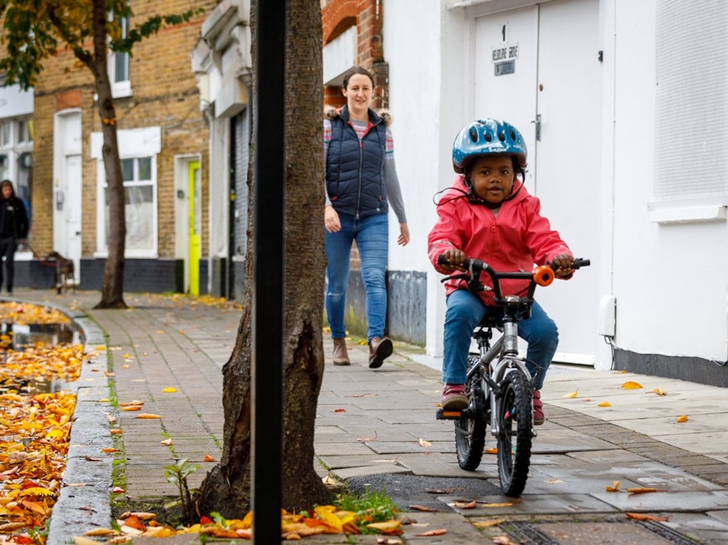 A woman walking down the street with a young child on a bicycle