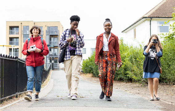 4 young people walk along the street, all of them are holding cameras