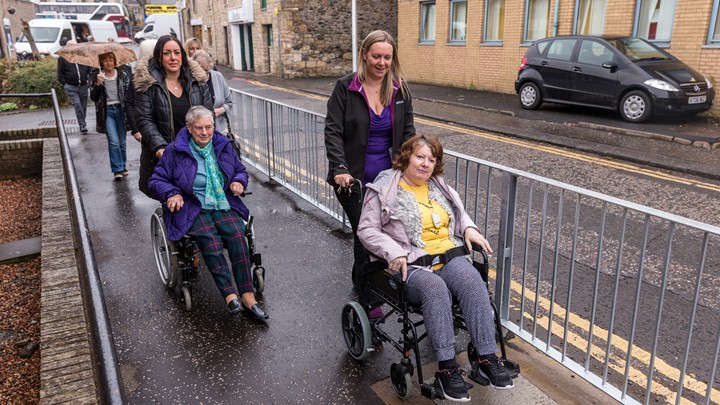 two older people in wheelchairs being pushed by two women