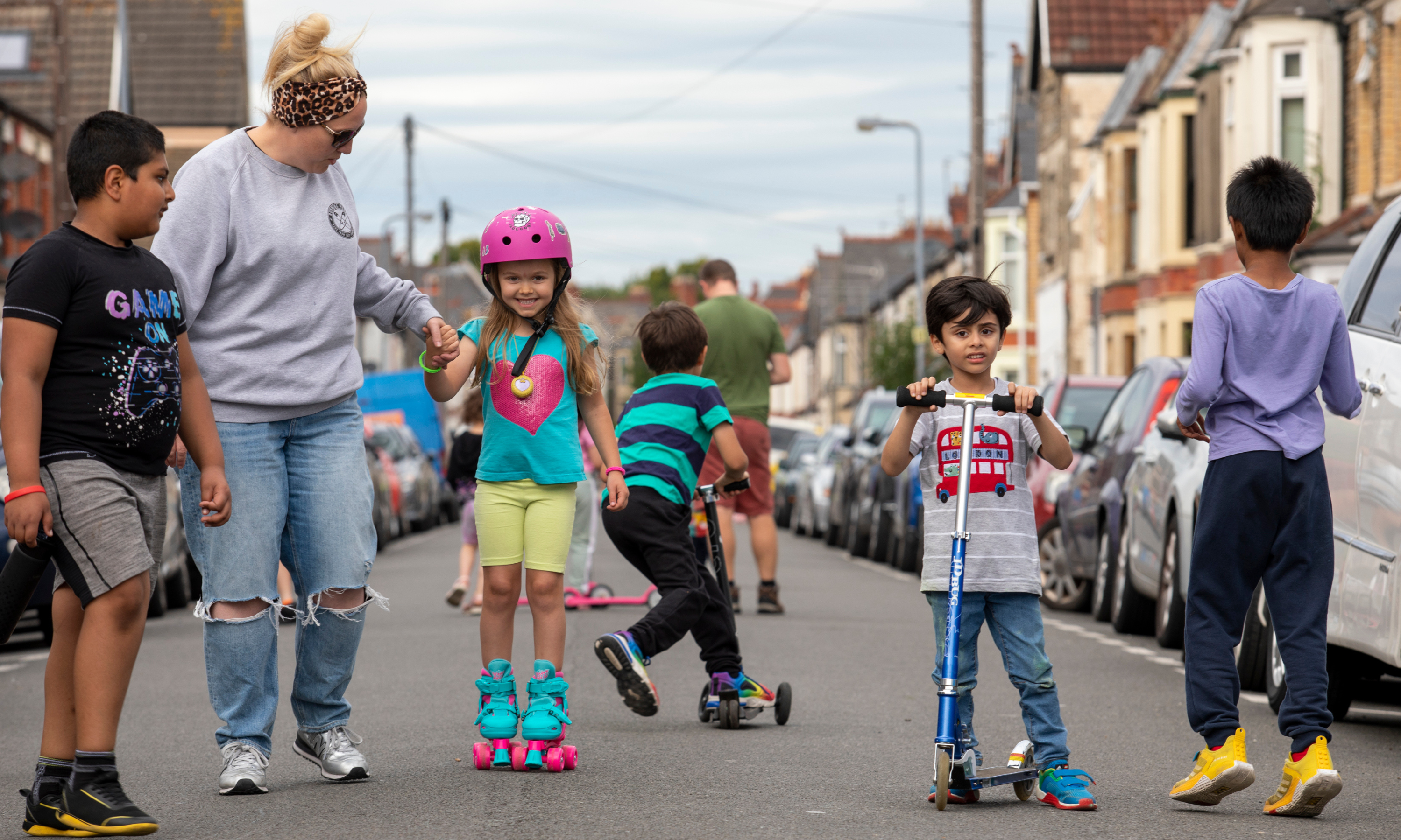 A group of children play on scooters and rollerskates in the street
