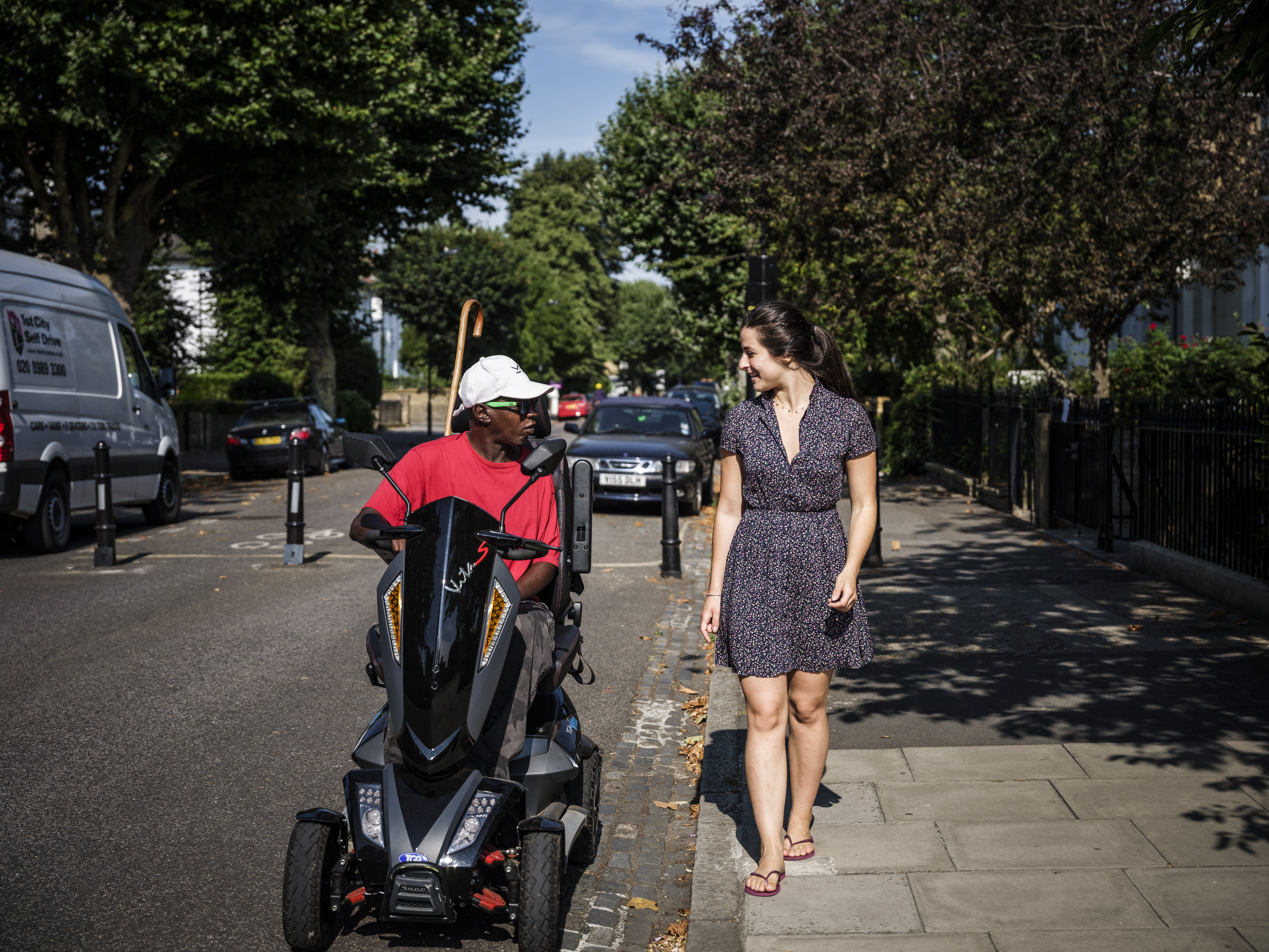 black man on a mobility scooter talks to a white woman on the pavement