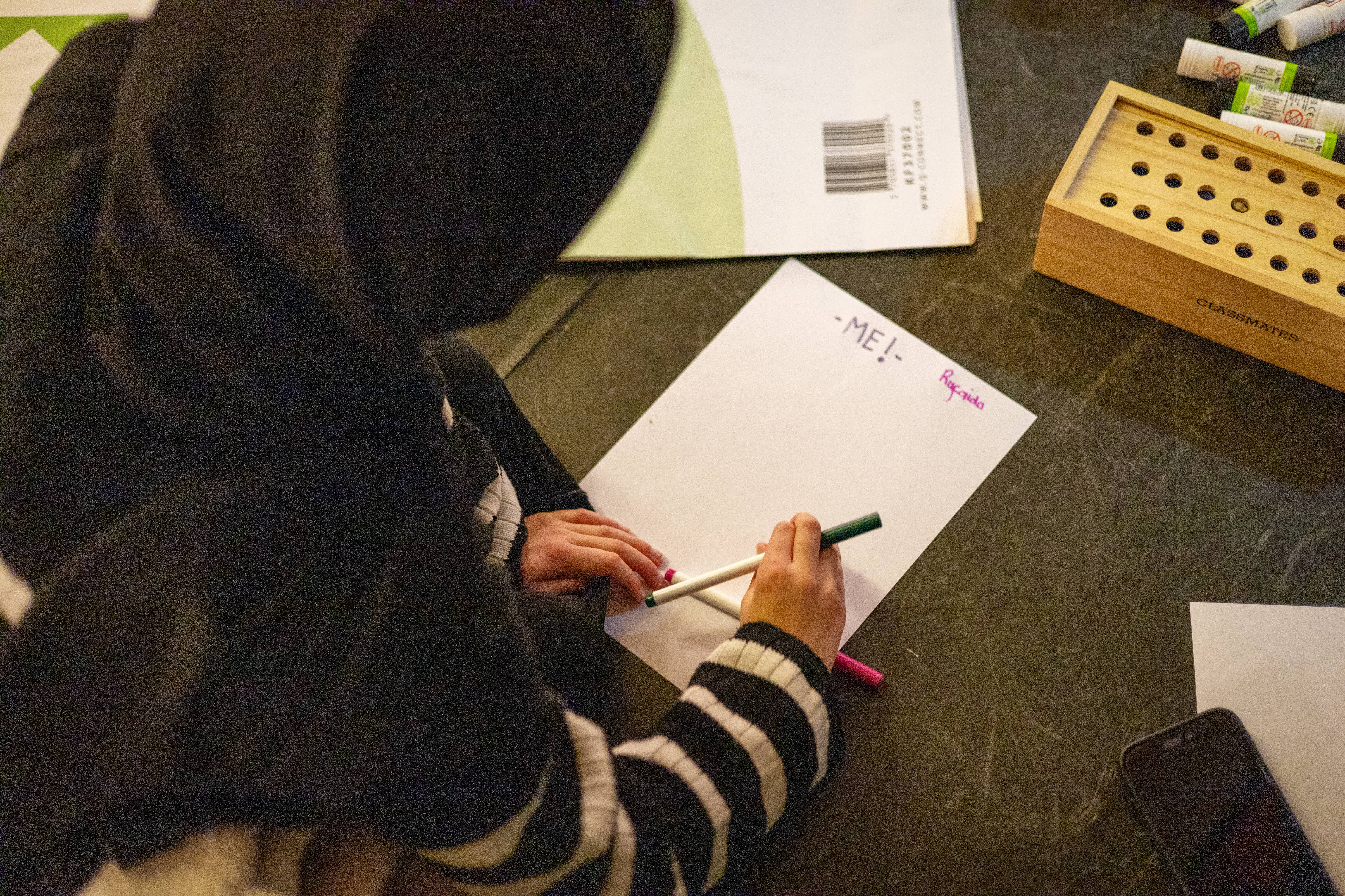 a girl is writing on a piece of paper that says 'me!'