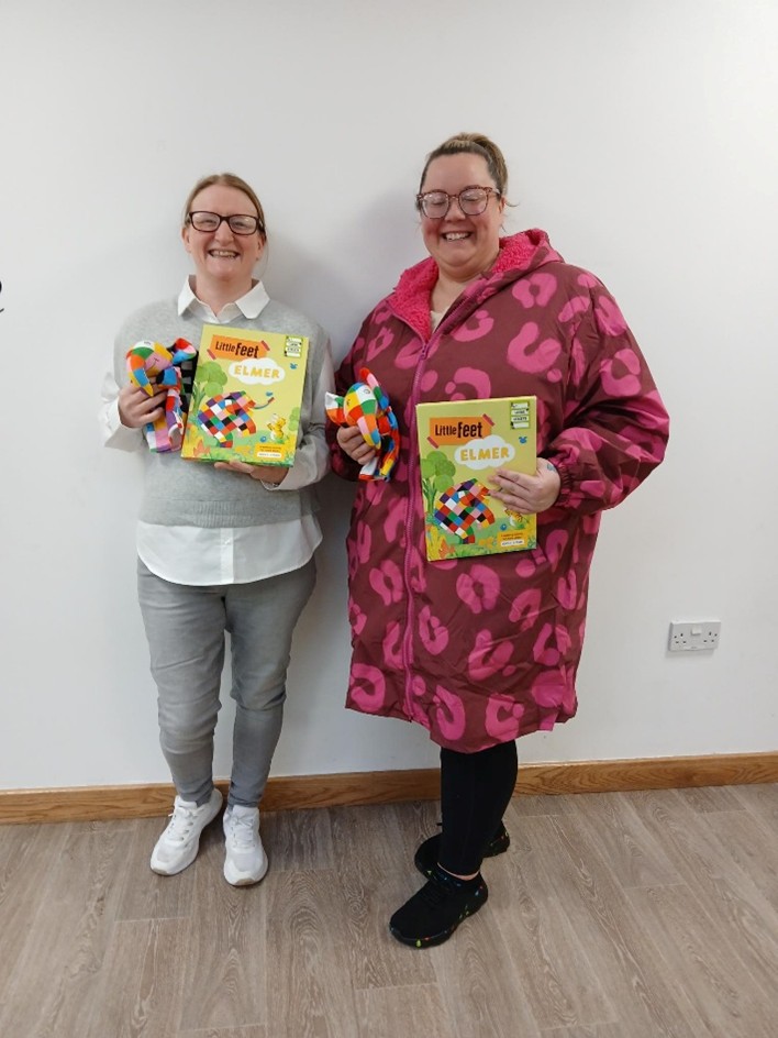 two people are seen smiling. They are holding Living Streets' Little Feet Elmer books.