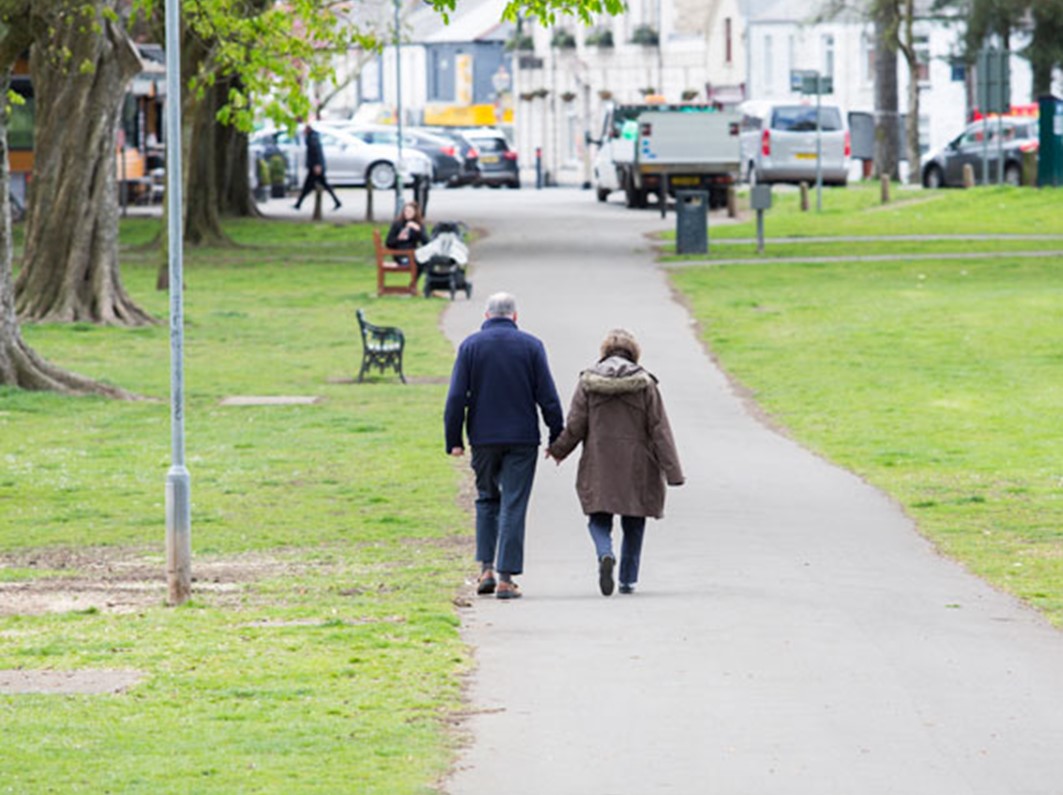 An older man and woman walking though a park