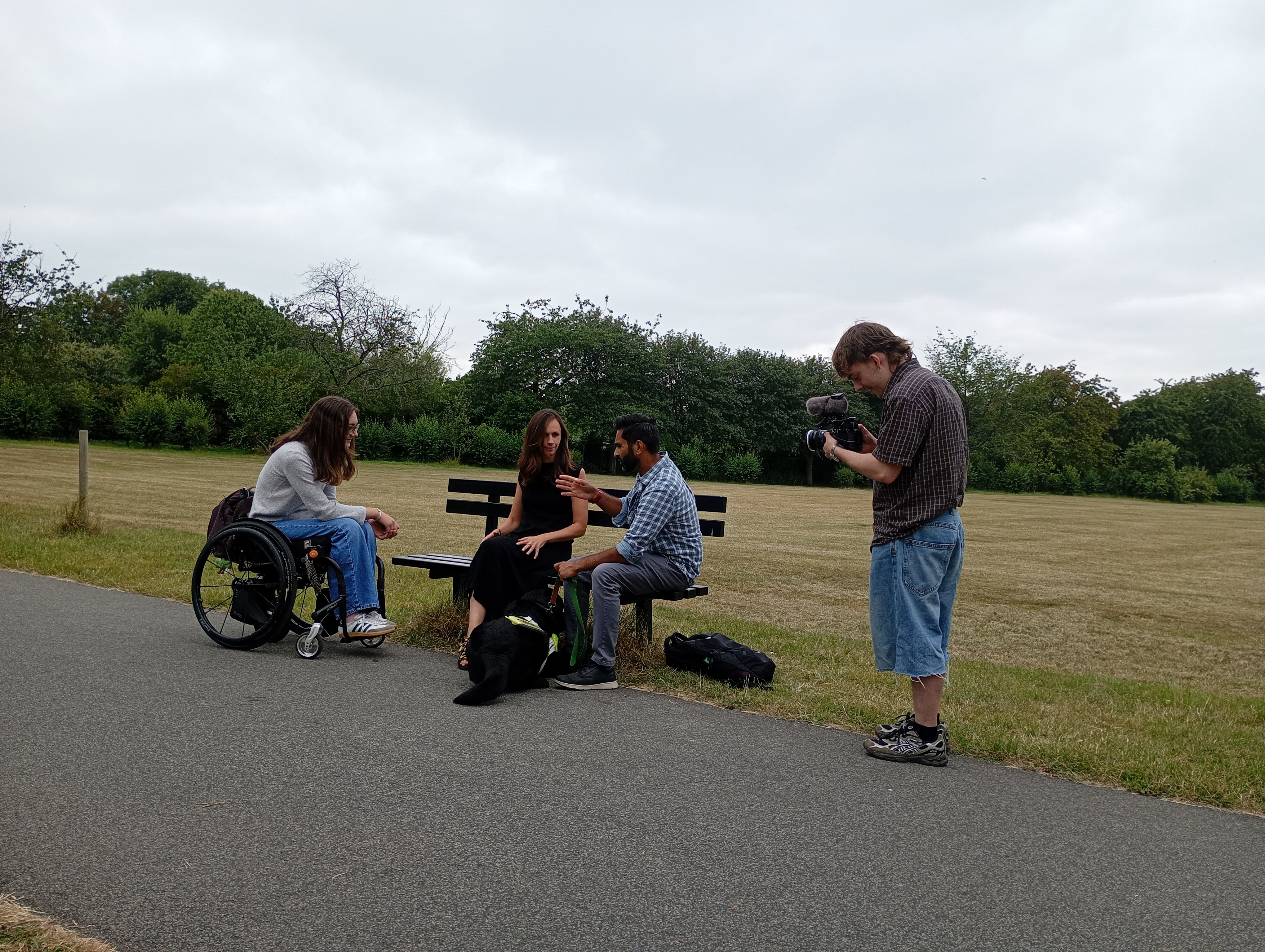 Emily, sat with two people and a guide dog being filmed in Leeds