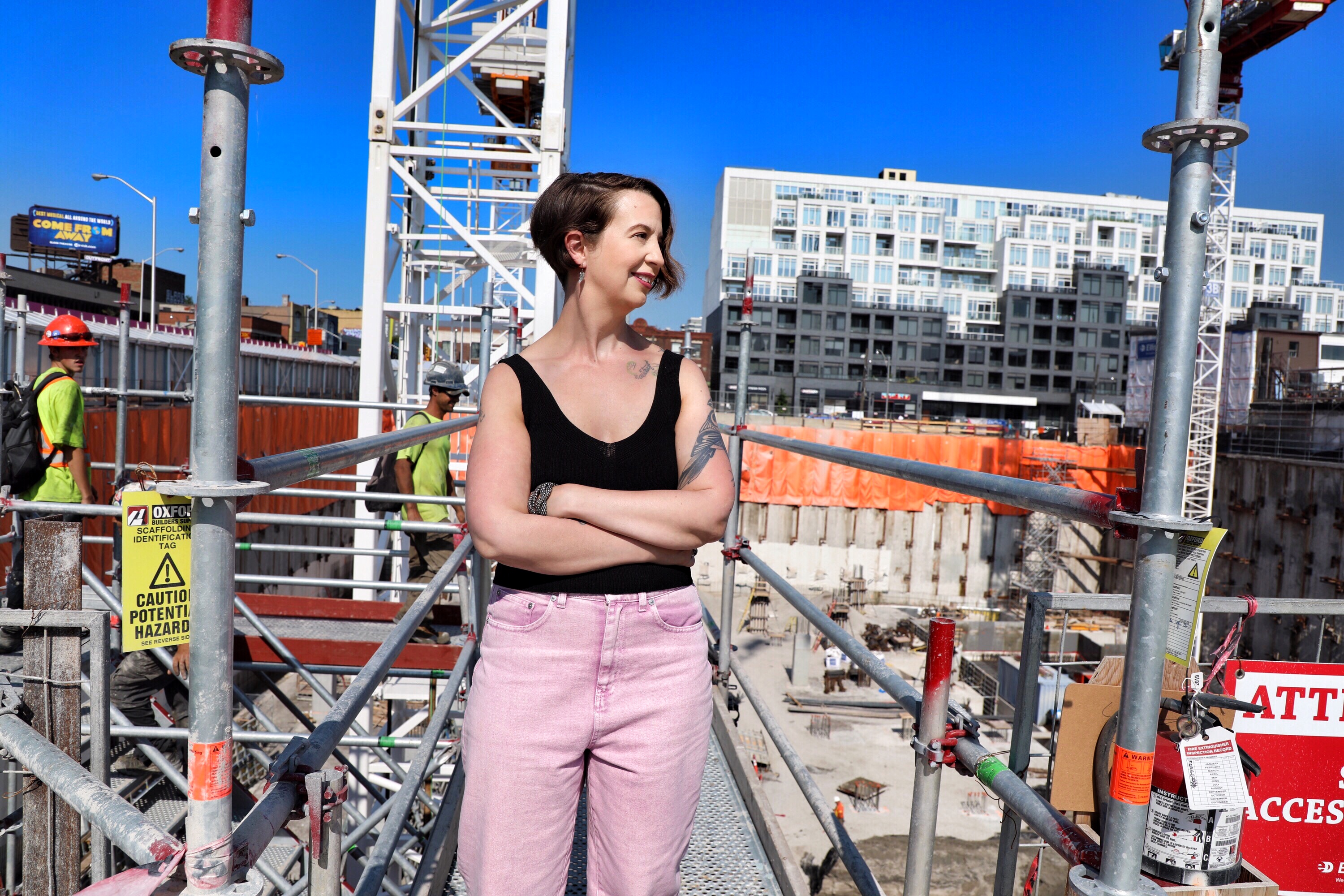 a woman wearing a black vest and pink jeans is standing on abuilding site