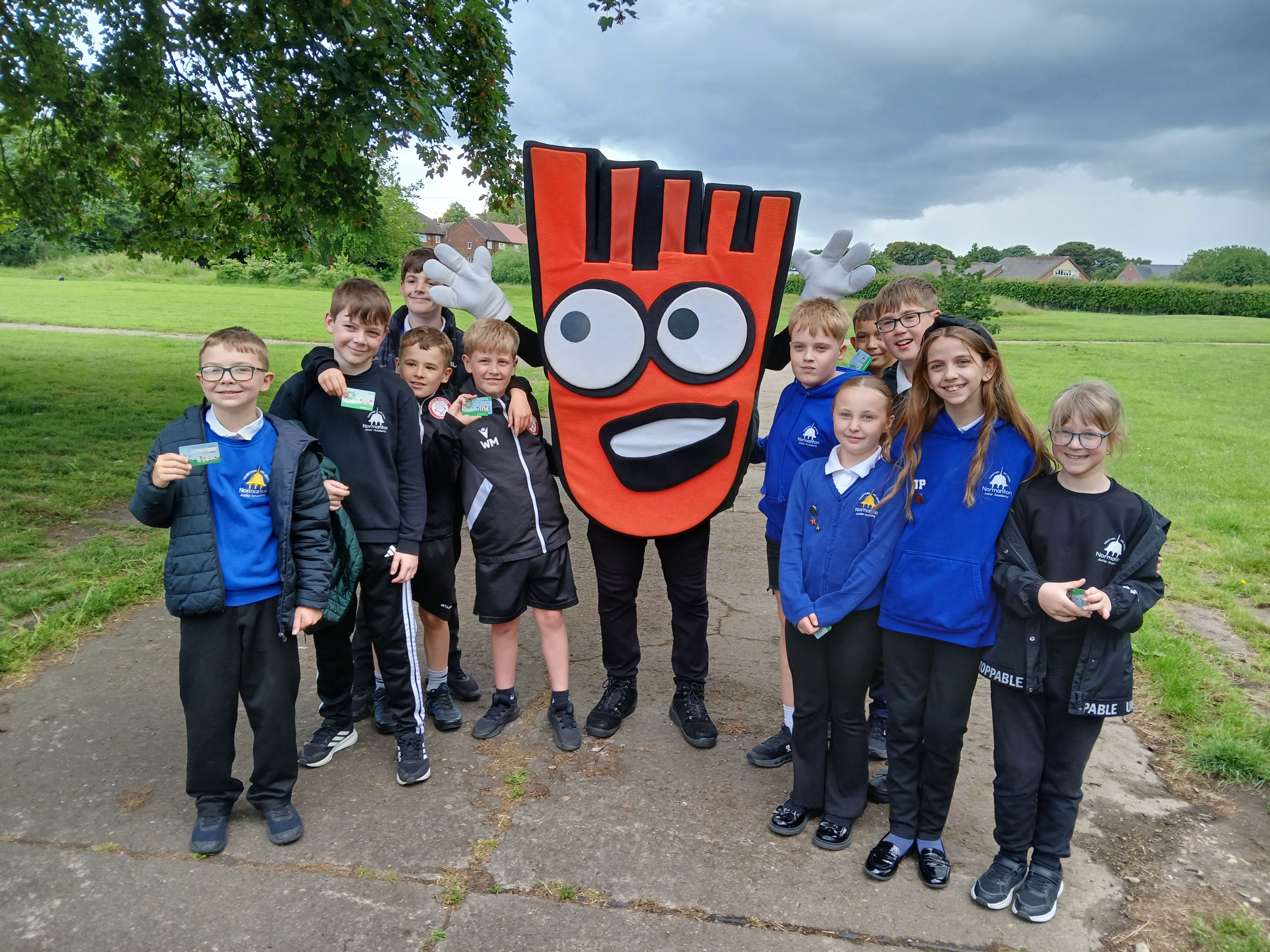 schoolchildren wearing blue uniforms stand on a path smiling with Strider, the Living Streets mascot