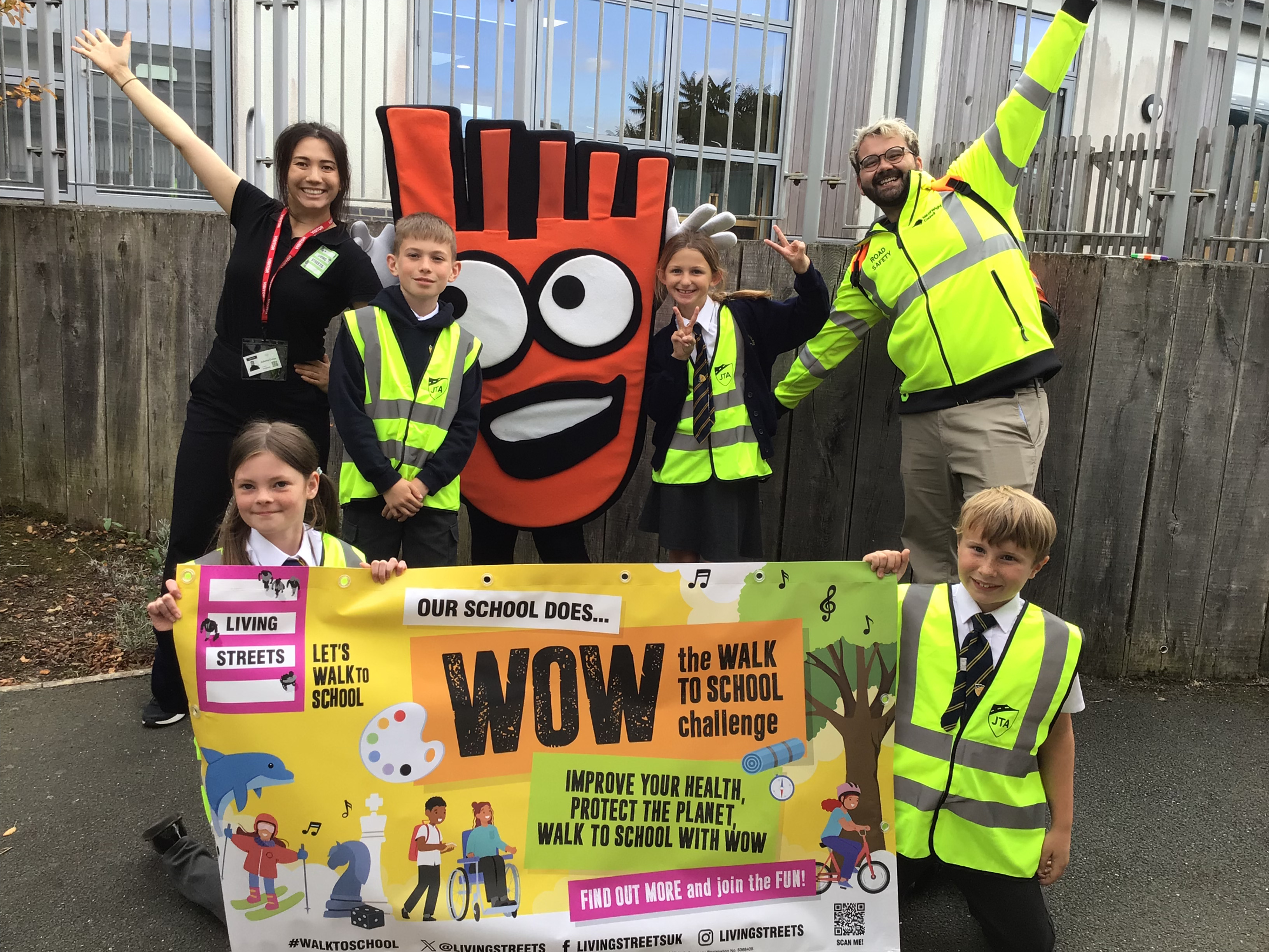 Four primary school aged pupils pose with a WOW banner, Strider - our giant orange foot mascot - and two adults from Living Streets and Isle of Wight Council. They are all smiling into the camera.
