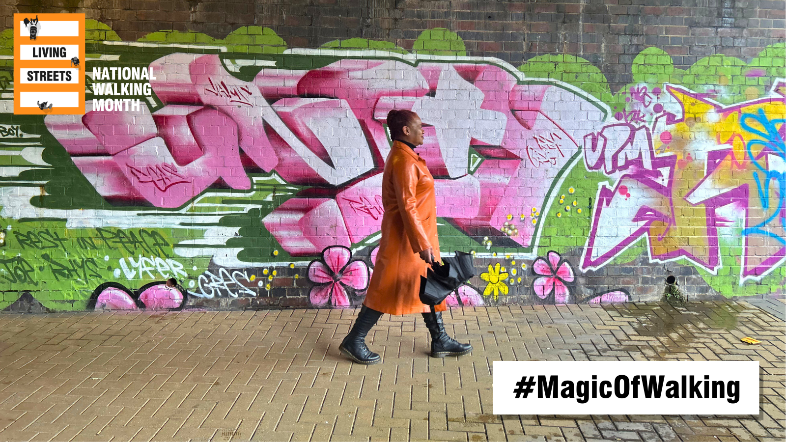 A woman in an orange coat walks past graffiti holding an umbrella