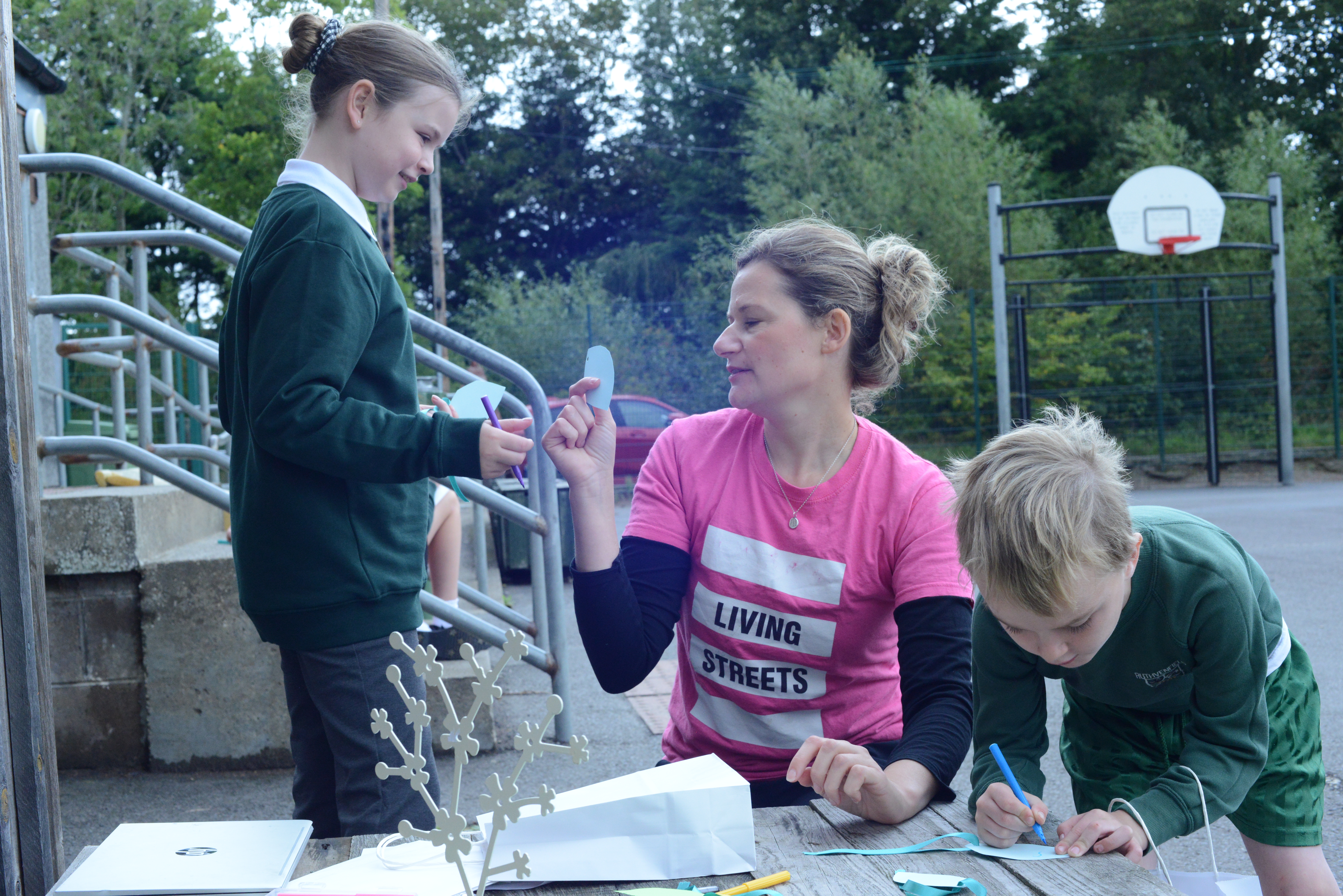 A woman and two school children are making crafts on a playground