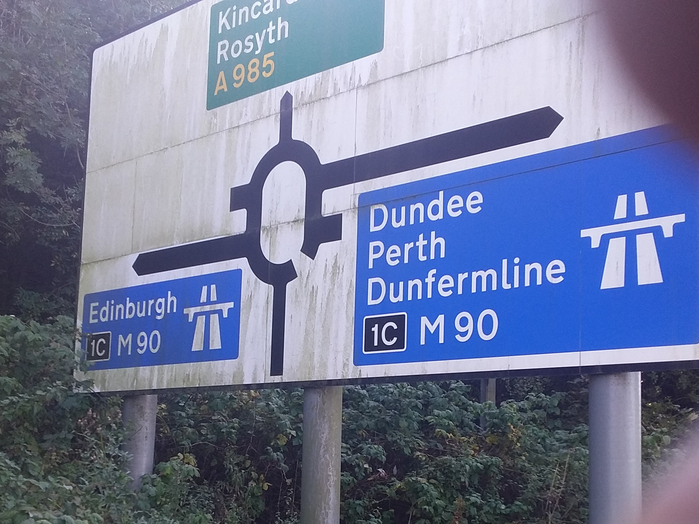 A photograph of a road sign for a roundabout. Different exits off the roundabout show Edinburgh, Rosyth, Dundee, Perth, and Dunfermline
