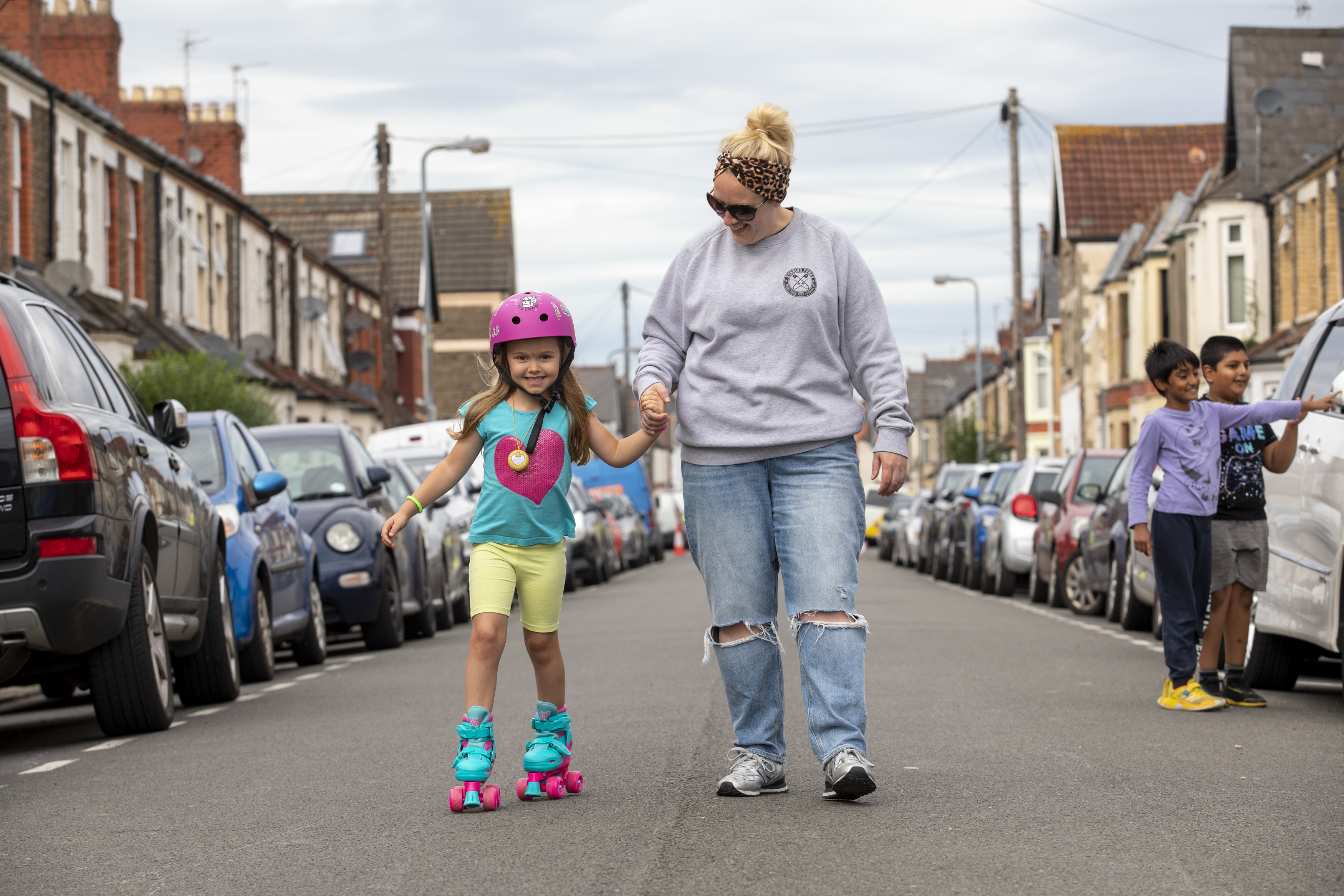 An adult helps a child to rollerskate down a carriageway