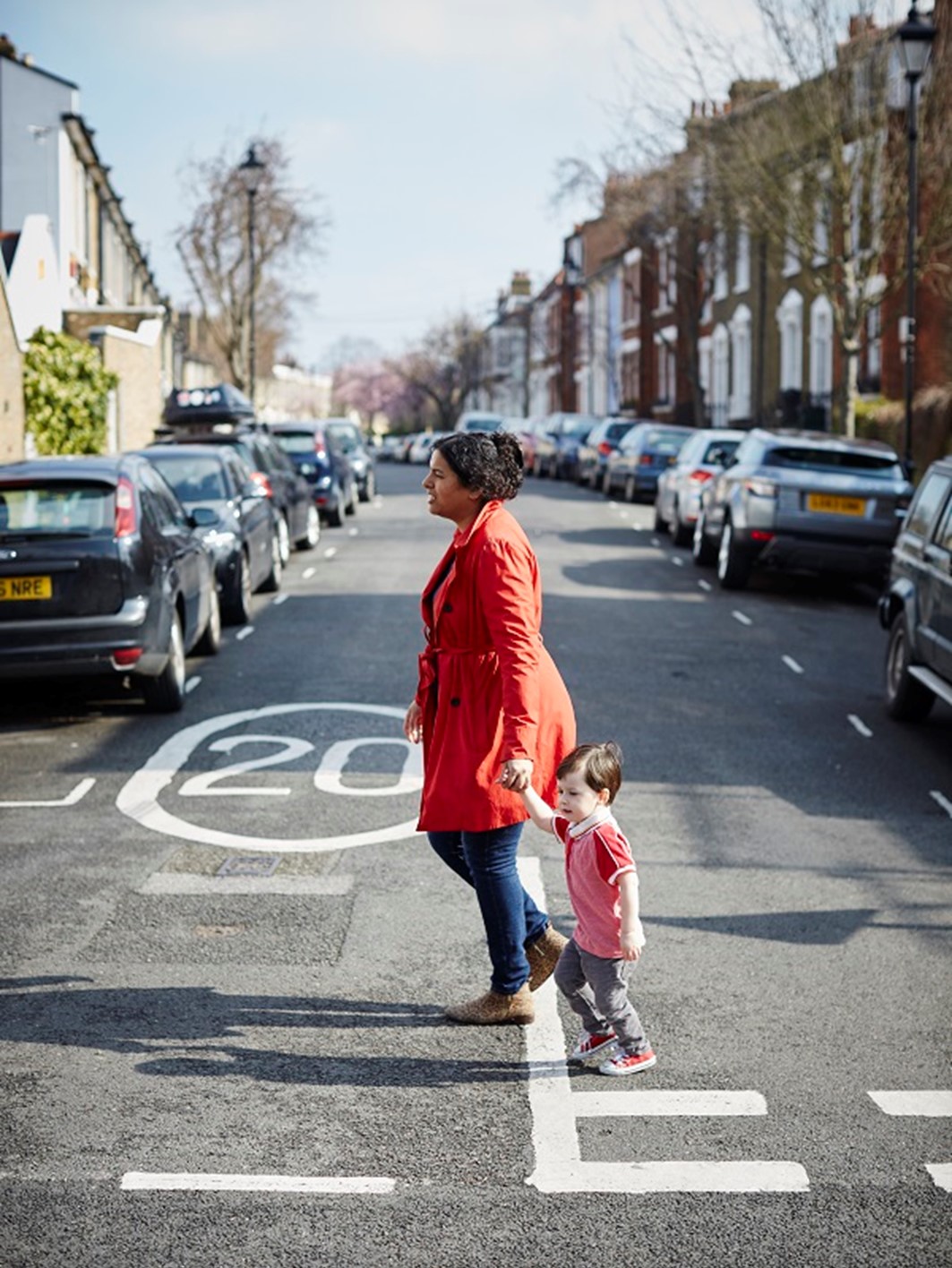 A parent and child walk across a road with a 20mph speed limit indicated
