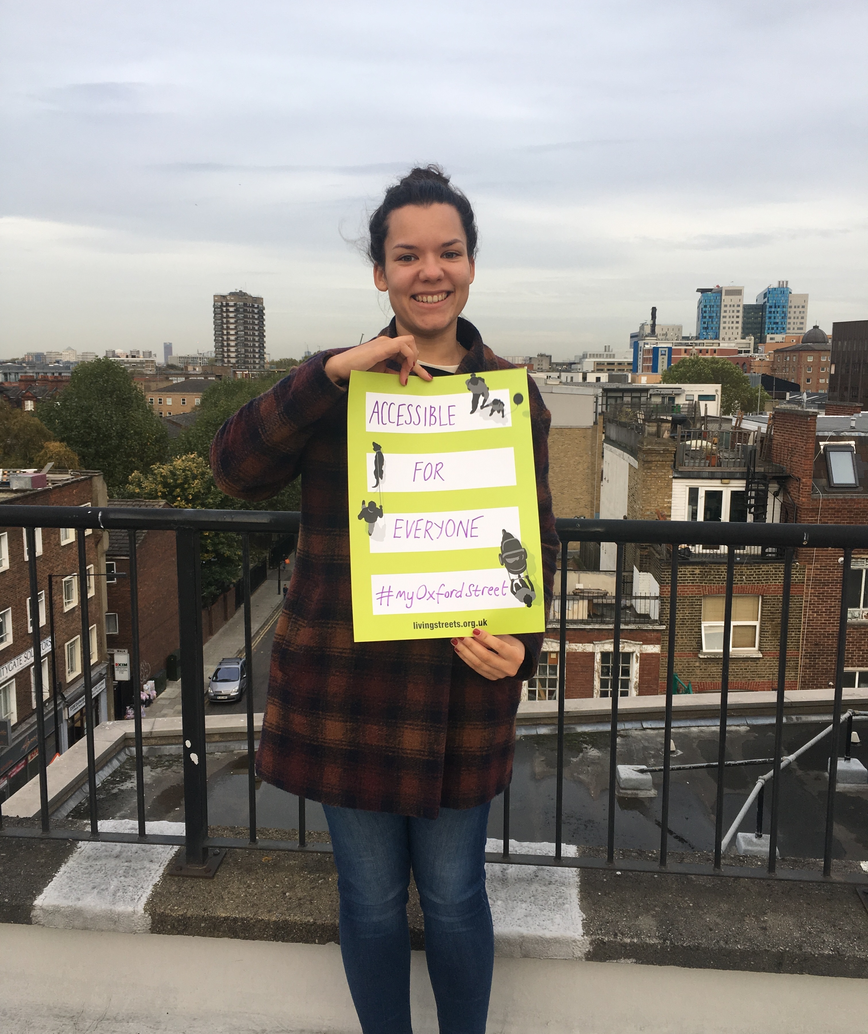 A woman with dark hair holds a sign that says: Accessible for everyone #MyOxfordStreet