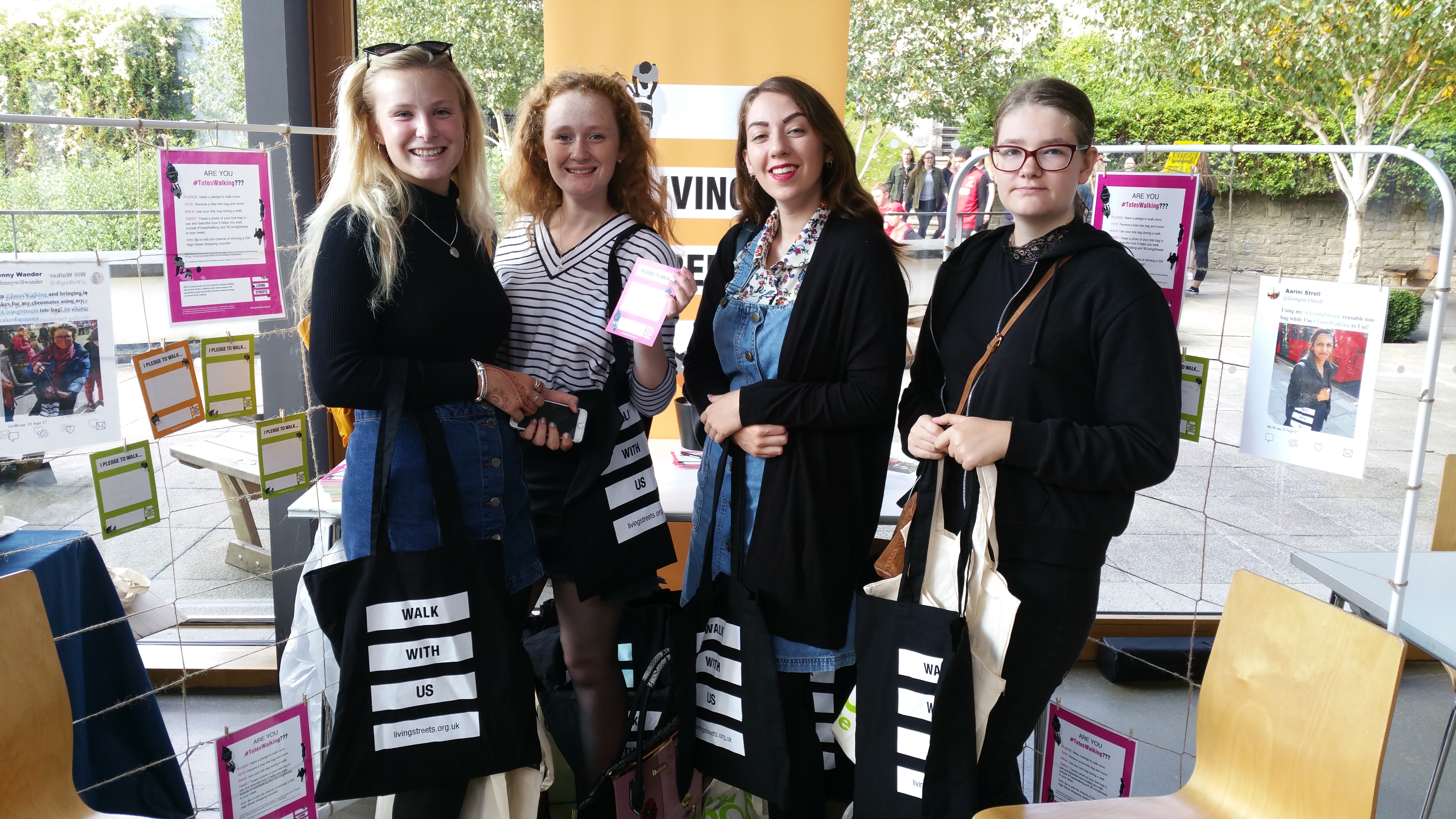 4 young women holding living streets merch and smiling