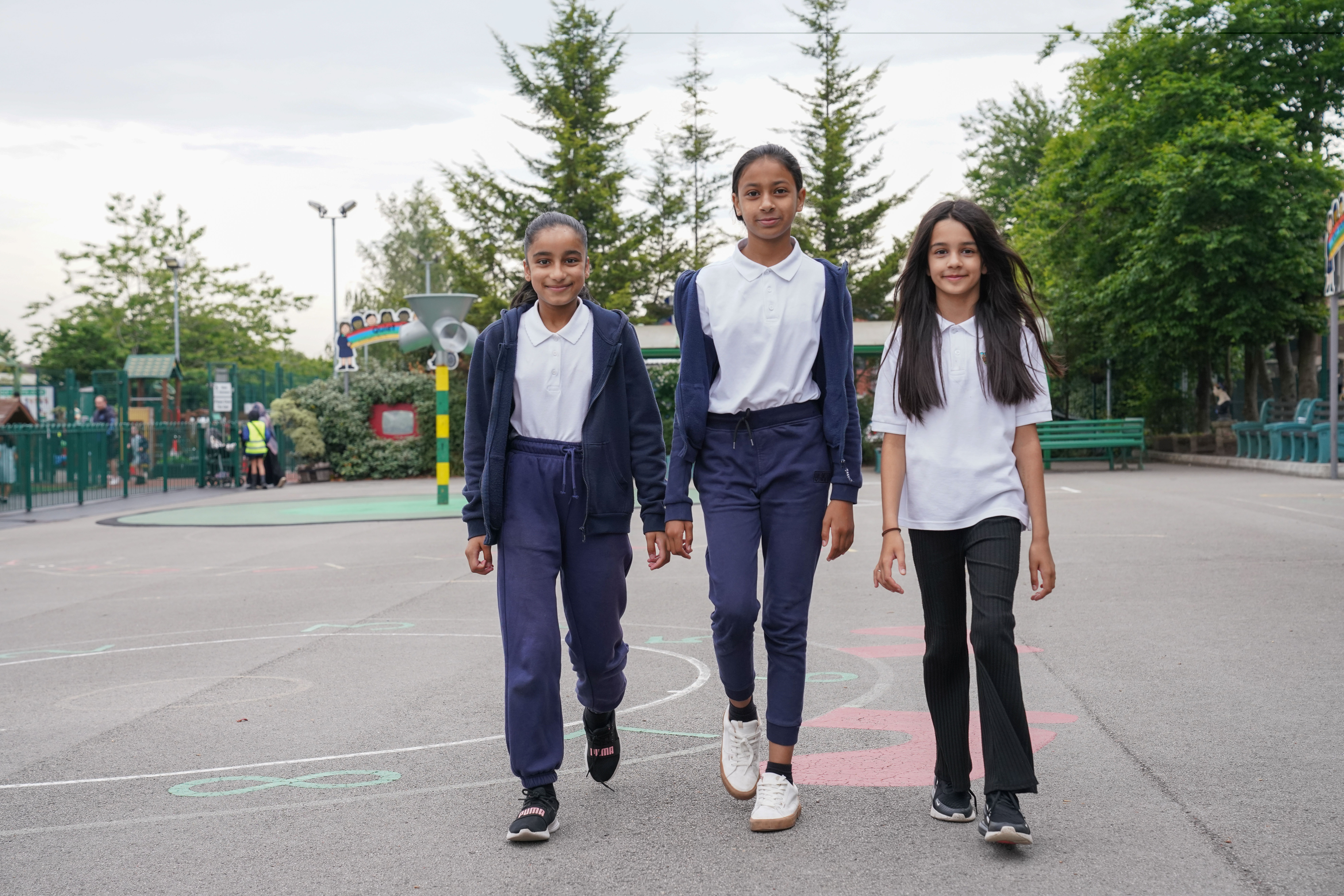 Three school children walk side by side in a playground