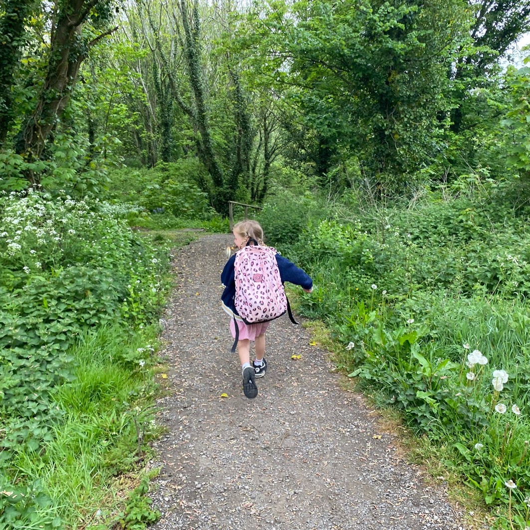 A young school girl runs through a grassy woodland path