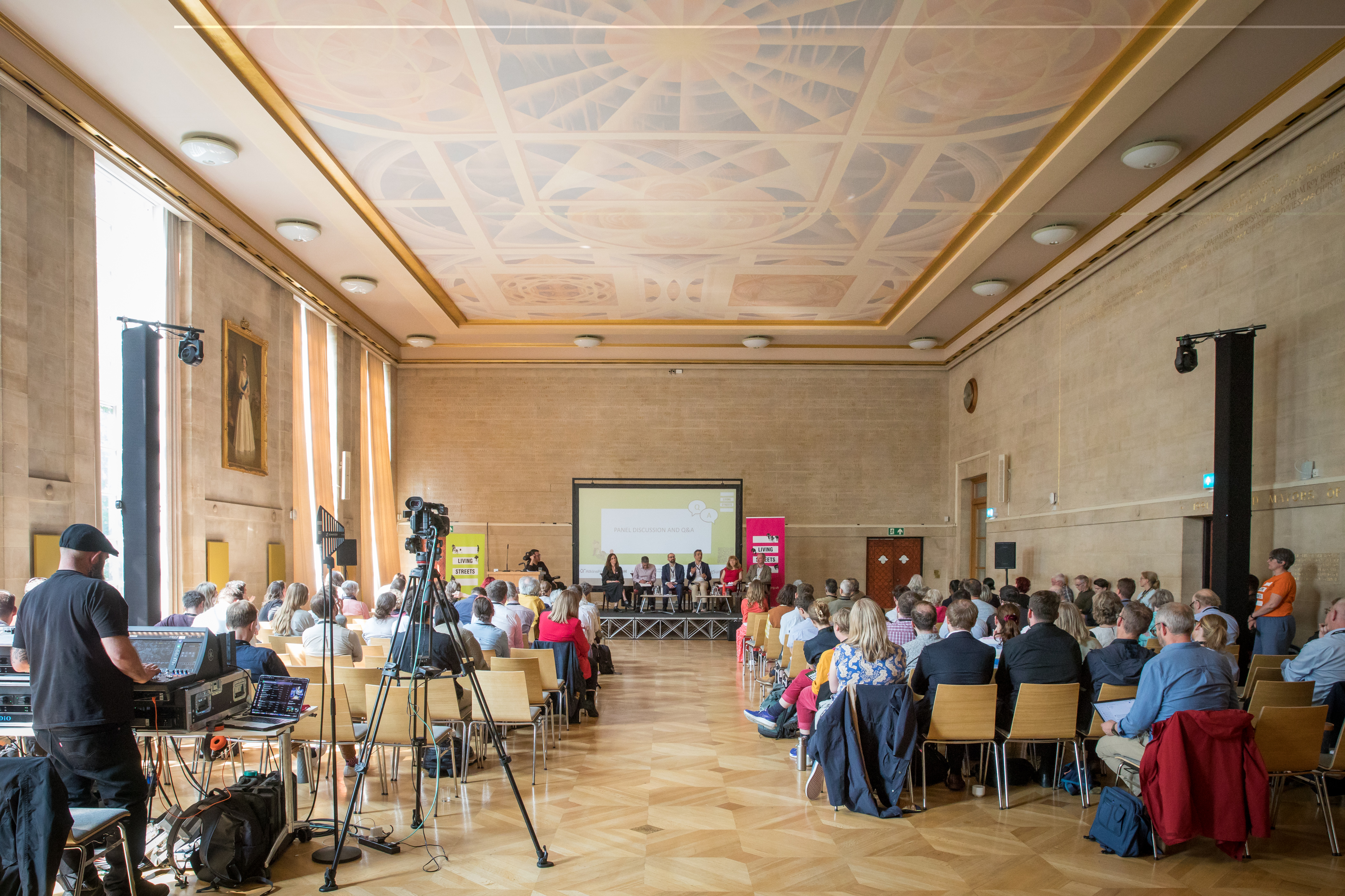 The UK Walking Summit 2025 takes place in a large hall, 7 people are seated on stage presenting to a room of 200 delegates