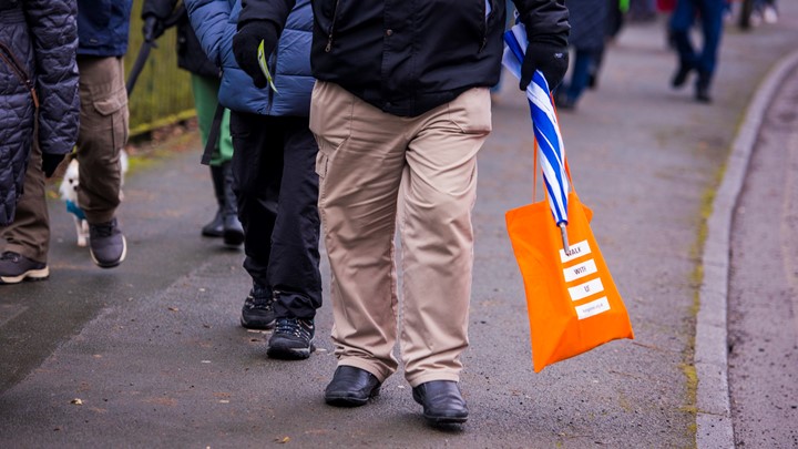 man walks along the road holding living streets bag and umbrella