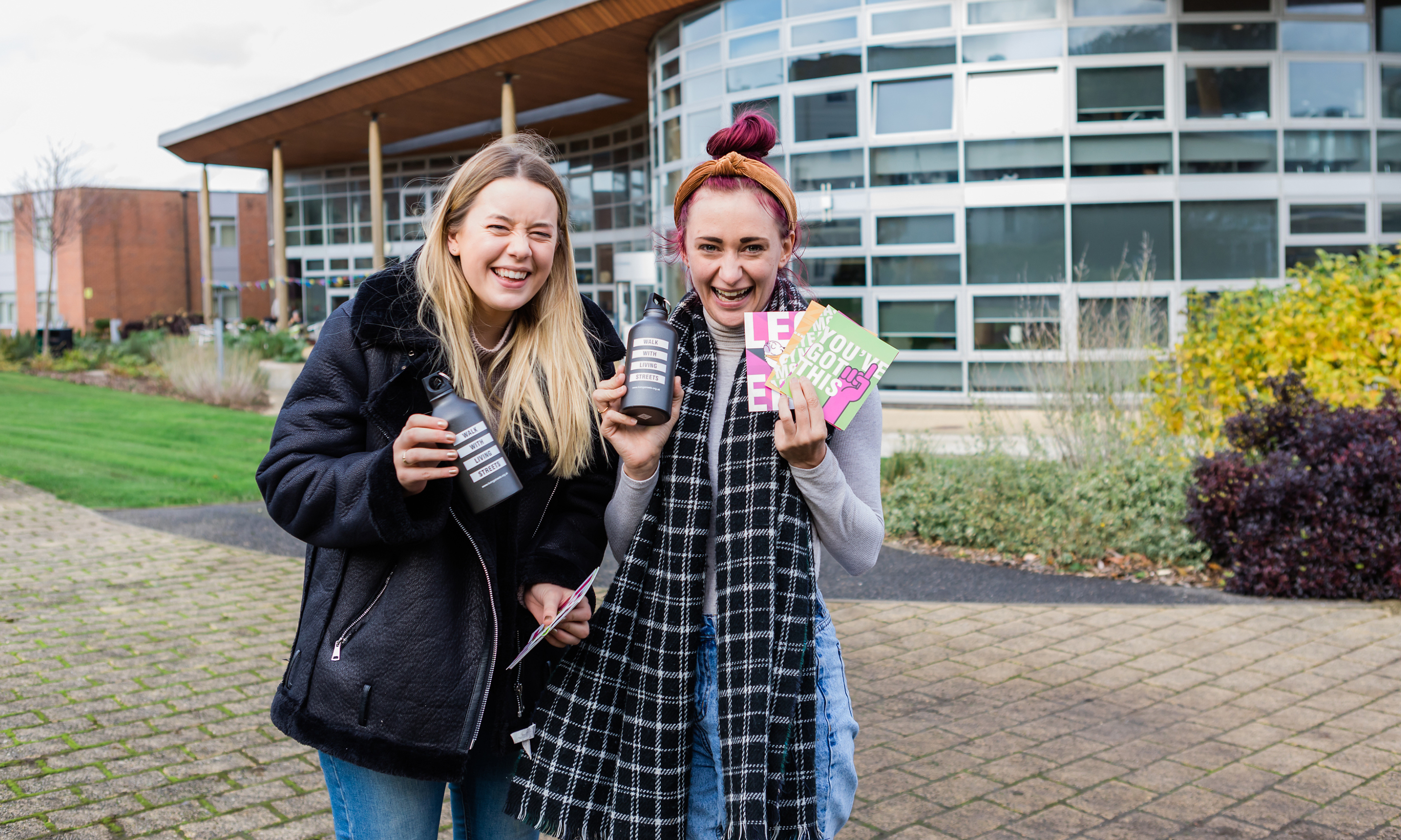 two student women holding up living streets merchandise and smiling