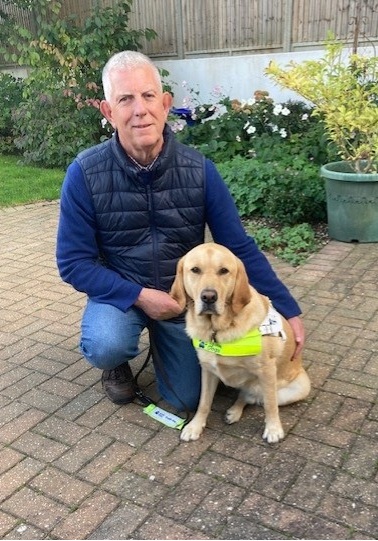 A photograph of a man knelt down next to his guide dog