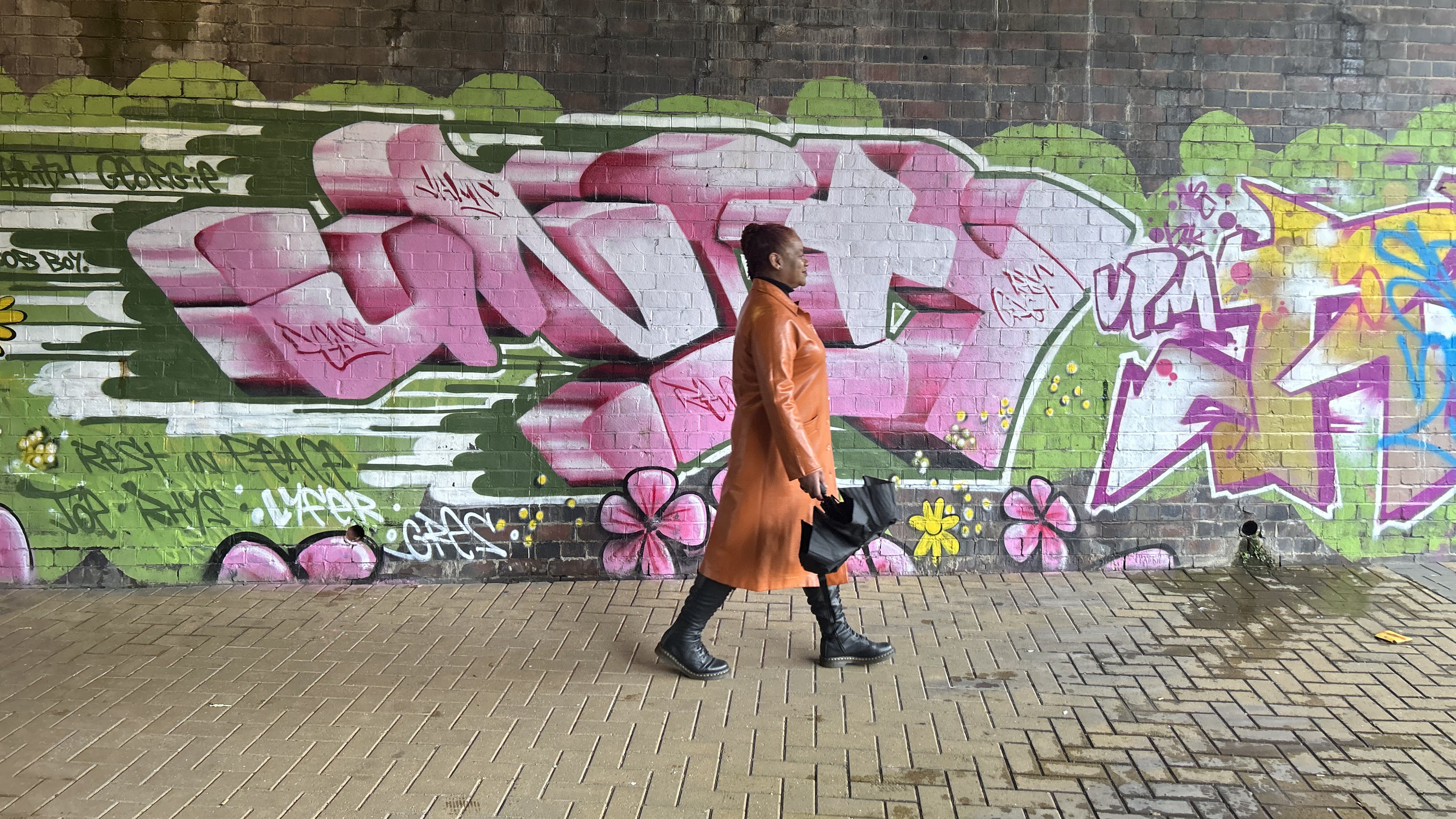 A woman walks in an underpass in front of a graffitied wall