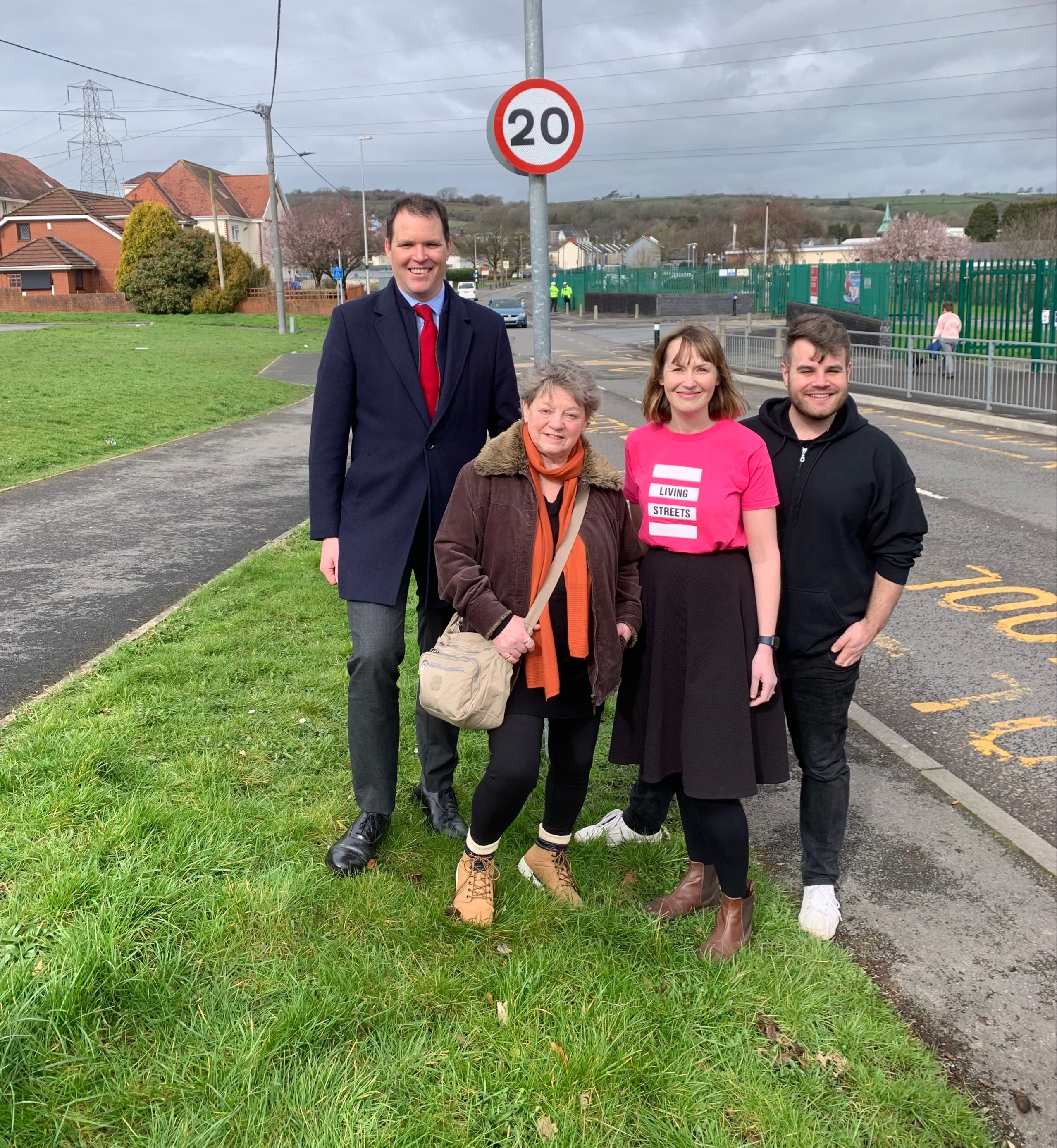 4 people stand by a 20mph sign including Josh and a woman wearing a pink Living Streets tshirt