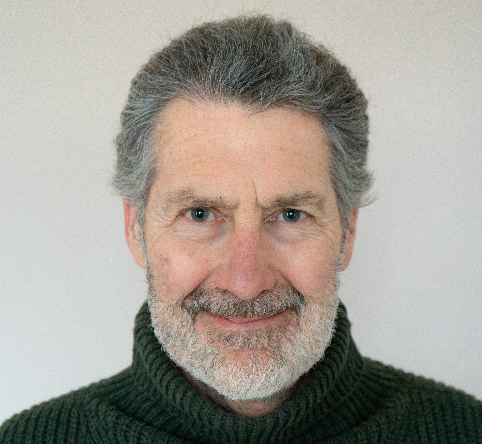 A photograph of Jeremy Leach: an older white man smiling at the camera and wearing a black jumper.