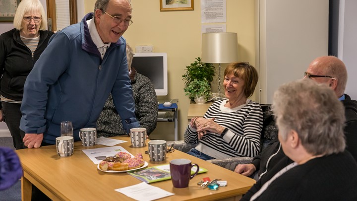 a group of older people sitting around table laughing with tea